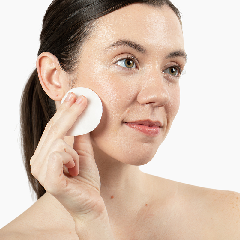 Woman applying Vivian Valenty Skincare cleanser to her cheek with a cotton pad for a fresh, healthy glow.