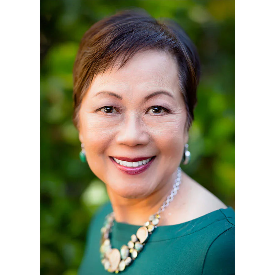 Vivian Valenty, founder of Vivian Valenty Skincare, smiling confidently in a green dress with red lipstick and a gold necklace.