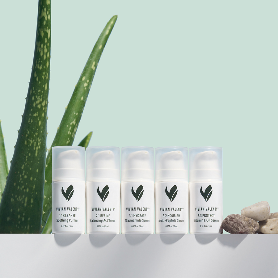 Vivian Valenty Skincare Kit displayed in a row next to a fresh aloe vera plant, highlighting natural and soothing ingredients.