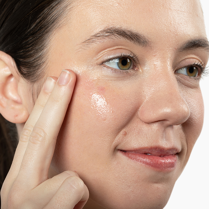 Woman applying Vivian Valenty Skincare cleanser to her cheek for a fresh, healthy glow.